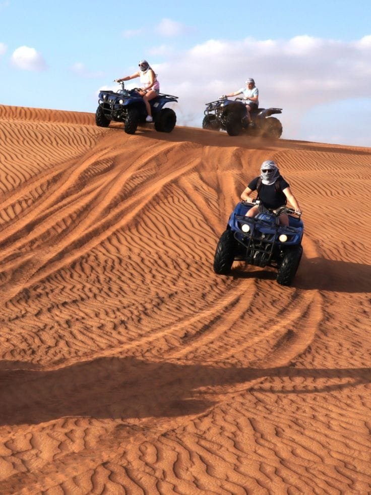 Tourist riding an ATV quad bike on the golden Al Khatim dunes during a Desert Safari in Abu Dhabi