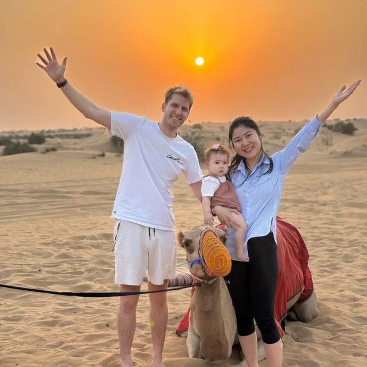 Smiling couple posing next to camel at a desert safari camp