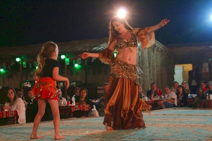 Woman guest with belly dancer at family desert safari camp Abu Dhabi