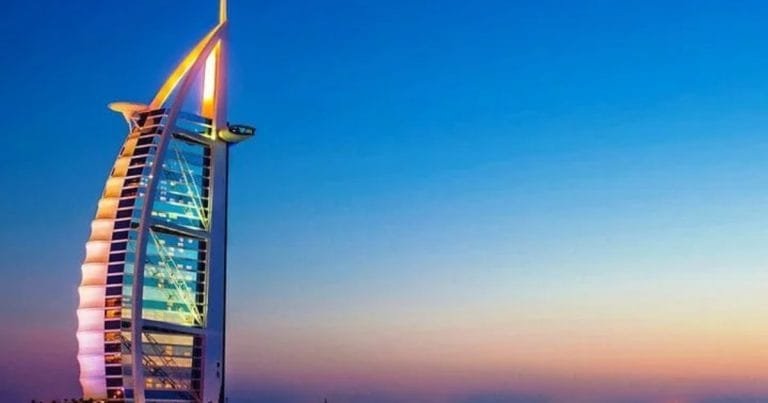 The sail-shaped Burj Al Arab hotel lit in colour against a dusk sky in Dubai