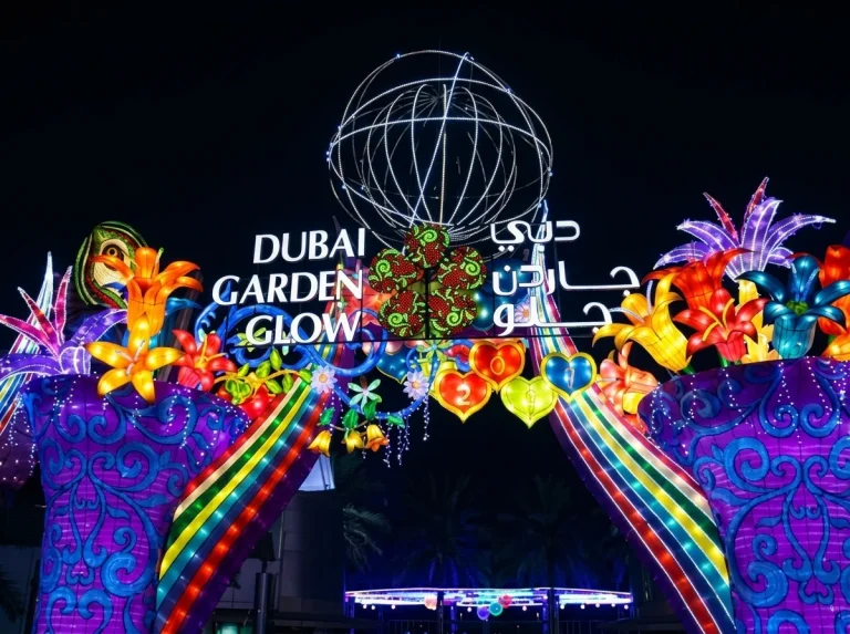 Illuminated Dubai Garden Glow entrance sign with rainbow arches and flower lanterns at night