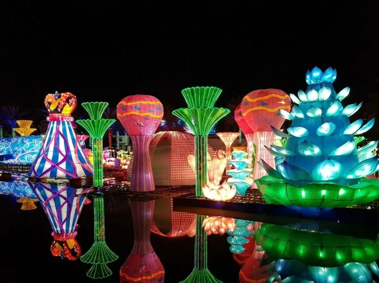 Glowing lotus and vase light sculptures mirrored in the water at Dubai Garden Glow