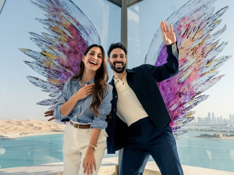 Happy couple posing at the Dubai wings art installation with palm views behind