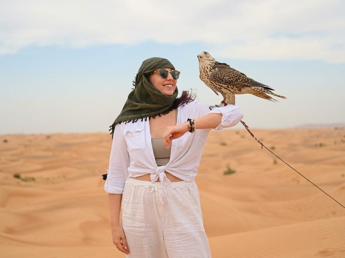 Guest holding a trained falcon on the dunes during an Abu Dhabi stopover desert safari