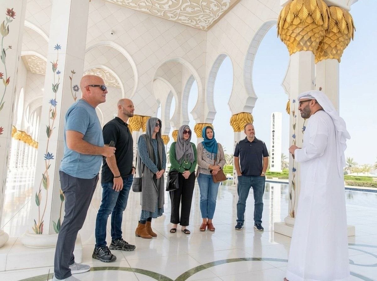 Guide in kandura showing guests the courtyard arches of Sheikh Zayed Grand Mosque on an Abu Dhabi stopover tour
