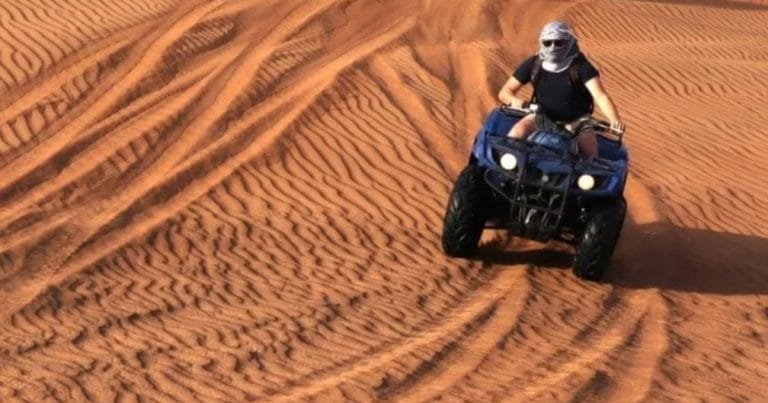 Quad bike rider climbing a golden dune at the desert